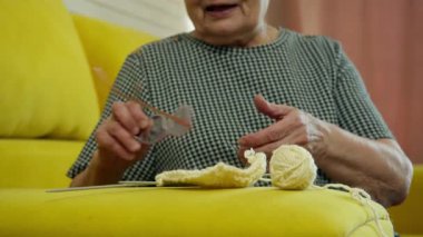 Kıdemli kadın rahat sarı bir kanepede örgü örmeyi seviyor.