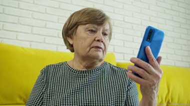 Video için akıllı telefon kullanan, telefonla konuşan, sarı koltukta oturan yaşlı bir kadın.