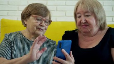 İki son sınıf öğrencisi sarı bir kanepede oturup akıllı telefon kullanarak video görüşmesi yapıyorlar.