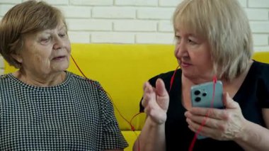 Kulaklıkla müzik dinleyen, akıllı telefonu paylaşan ve gülen iki son sınıf öğrencisi kadın.