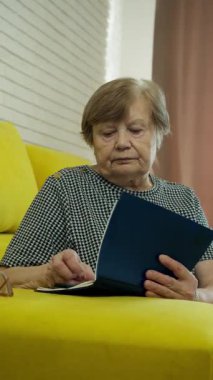 Yaşlı kadın rahat sarı bir kanepede dinleniyor, kitap açıp okuyor.