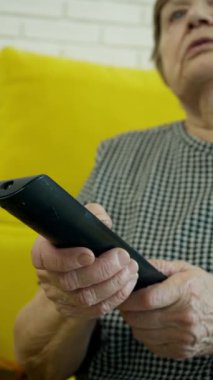 Üst düzey kadın uzaktan kumanda kullanıyor, koltukta oturuyor, televizyon seyrediyor.