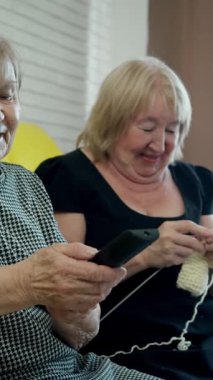 İki yaşlı kadın boş zamanın keyfini çıkarıyor, biri televizyon seyrediyor ve diğeri örgü örüyor.