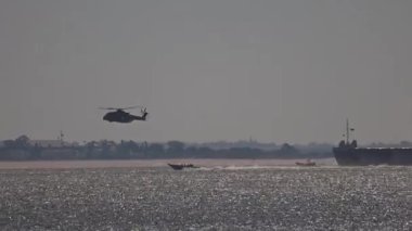 Askeri helikopter bir sürat teknesi ve bir savaş gemisinin üzerinde alçaktan uçuyor.