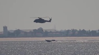 Deniz tatbikatı sırasında hızlı bir teknenin yanında uçan askeri helikopter.