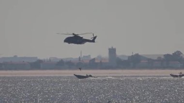 Askeri helikopter bir motorbotun yanında denizin üzerinde uçuyor.