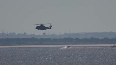 Bir tekne yaklaşırken askeri helikopter denizden halatla bir kişiyi çıkarıyor.