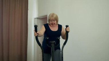 Oturma odasında eliptik makine üzerinde egzersiz yapan yaşlı bir kadın.