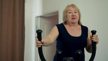 Yaşlı bir kadın dairesinde eliptik bir makine kullanarak formunu geliştiriyor.