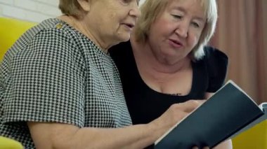 İki mutlu yaşlı kadın birlikte kitap okuyor ve gülümsüyor.