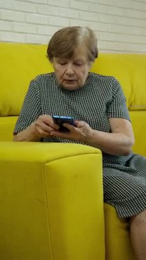 Üst düzey bir kadın sarı bir koltukta otururken telefonla konuşuyor.