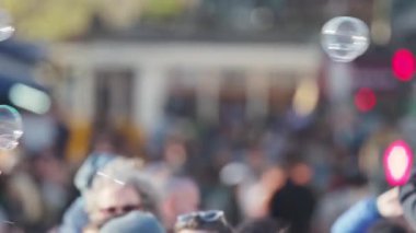 Şehir caddesinde yürüyen bulanık kalabalığın üzerinde sabun köpükleri yüzüyor.