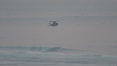 Hava bulutluyken dalgalı bir okyanusta devriye gezen askeri helikopter.