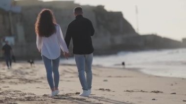 Gün batımında kumsalda romantik yürüyüşlerin tadını çıkaran genç bir çift.