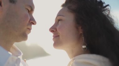 Romantik çift hassas bir anın tadını çıkarıyor, yüzleri birbirine yakın, batan güneşin sıcacık parıltısıyla aydınlanıyor.