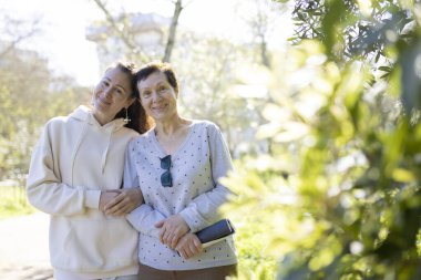 Gülümseyen anne ve kız parkta sarılıyor, güneşli bir günün tadını çıkarıyor.