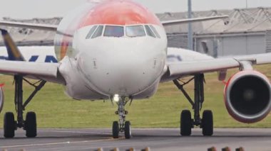 Beyaz ve turuncu yolcu uçağı bir havaalanı pistinde taksicilik yapıyor.