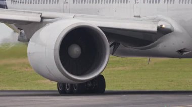 Modern bir yolcu uçağının motoru ve iniş takımı bir havaalanı pistinde taksicilik yaparken uzanıyor.