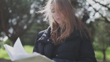 Rüzgâr, parkta kitap okurken genç bir kadının saçlarında hafifçe esiyor.