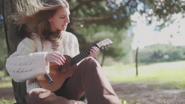 Parktaki bir ağacın altında akustik gitarını akort eden bir genç.