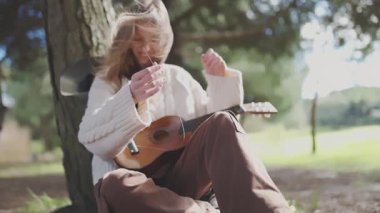 Rüzgarlı bir günde bir ağacın altında ukulele akort eden genç bir müzisyen