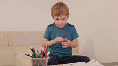 Evde renkli kalemlerle kağıda resim çizen konsantre çocuk.