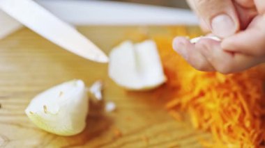 Ahşap kesim tahtasında rendelenmiş havuçların yanında beyaz soğan doğrayan şefin ellerine yakın durun.