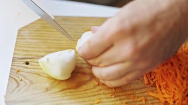 Aşçı ellerinin, rendelenmiş havuç ve soyulmuş patatesin yanında ahşap kesme tahtasıyla soğan doğramasını kapat.