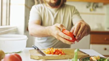 Adam yemek tarifi hazırlıyor. Mutfaktaki ahşap kesme tahtasıyla portakal dolmalık biber kesiyor.