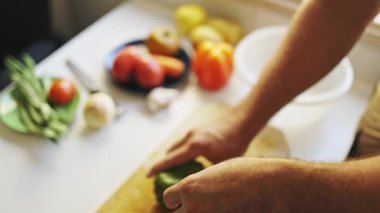 Şef, taze sebzelerle çevrili ahşap kesme tahtasına yeşil dolma biber dilimler.