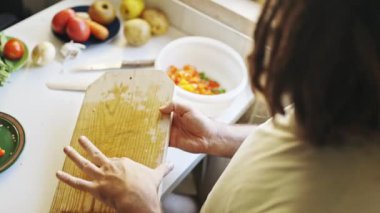 Mutfakta ahşap tahtada domates kesen bir adam.