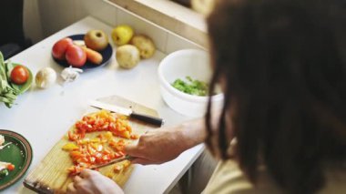 Mutfakta ahşap bir tahtanın üzerinde taze sebzeleri doğrayan bir aşçı.