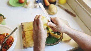 Şef, tahta kesme tahtasındaki bıçakla patates soyarken sağlıklı bir yemek için gerekli malzemeleri hazırlıyor.