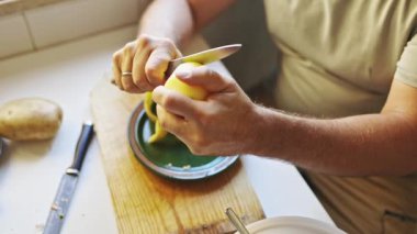 Ahşap kesme tahtasındaki bıçakla patates soyan şef.