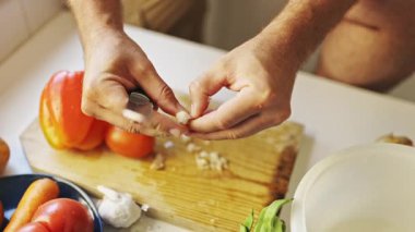 Şef sarımsak soyarken kesme tahtasının üzerinde, taze sebzelerle çevrili.