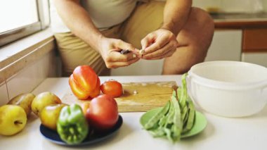 Şef sarımsak karanfillerini bıçakla soyuyor mutfakta tahtayı taze sebzelerle kesiyor.