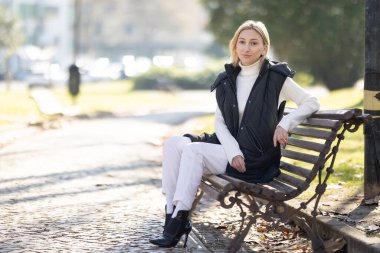 Şık bir kadın şehir parkında güneşli havanın tadını çıkarıyor, modern moda ve huzurlu şehir hayatını sergiliyor.