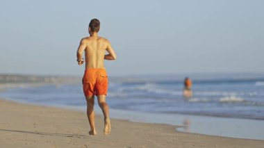 Genç atletik cankurtaran kıyı boyunca koşuyor.