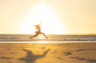 Zarif balerinin silueti canlı bir günbatımında sahile atlıyor.