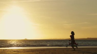 Genç kadın gün batımında sahilde dans edip koşuyor.
