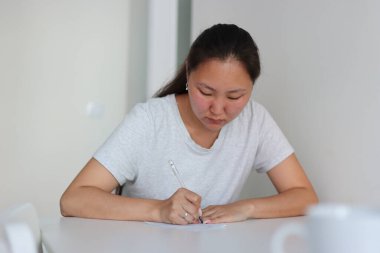 Asyalı etnik kökenli kadın, evinde beyaz bir kağıda yazı yazıyor.