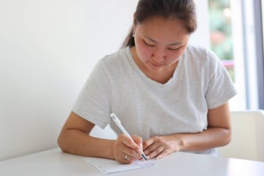 Asyalı bir kadın not defterine not alıyor, haftasını düzenliyor ve randevularını yazıyor.