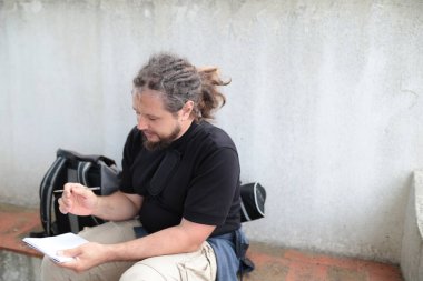 Erkek gazeteci dışarıda otururken not defterine not alıyor, muhtemelen haber yapmaya ara verdiği sırada.