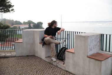 Fotoğrafçı ara veriyor ve Tagus nehri üzerindeki 25 de abril köprüsünü ve Lisbon 'un şehir manzarasını inceliyor.