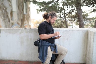 Erkek gazeteci dışarıda çalışırken not defterine not alıyor.