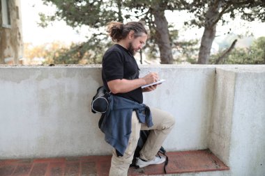 Erkek gazeteci ödevi için not defterine notlar yazıyor, günlük kıyafetler giyiyor.