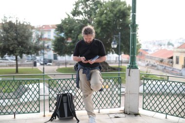 Sakallı turist akıllı telefon kullanıyor ve şehir parkında rehberlik yapıyor.