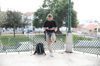 Lizbon, Portekiz 'de akıllı telefon kullanan erkek turist. Sırt çantası korkuluklara dayanıp manzaranın tadını çıkarıyor.