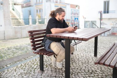 Portekiz 'deki açık hava masasında akıllı telefon kullanan sakallı turist.