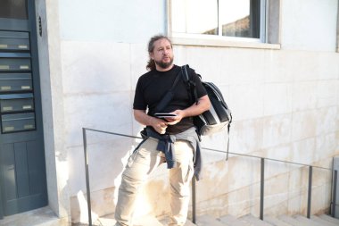 Sırt çantası ve pasaportuyla şehri keşfeden erkek turist, elinde akıllı bir telefon tutuyor.